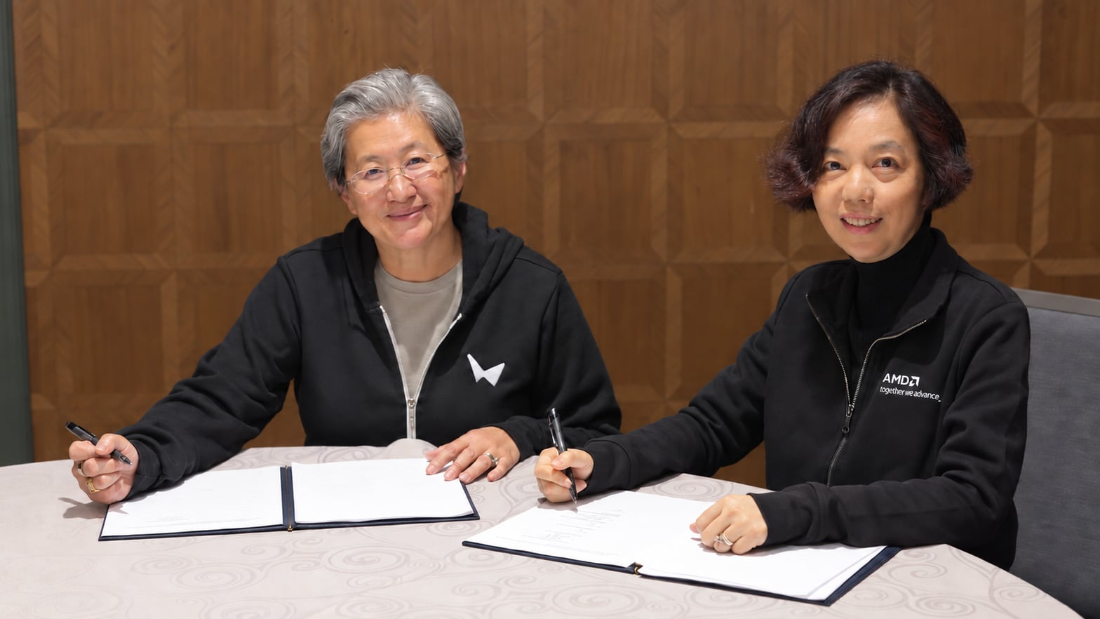 AMD CEO Lisa Su and World Labs founder Fei-Fei Li signing the acquisition agreement, each wearing the other company's jacket