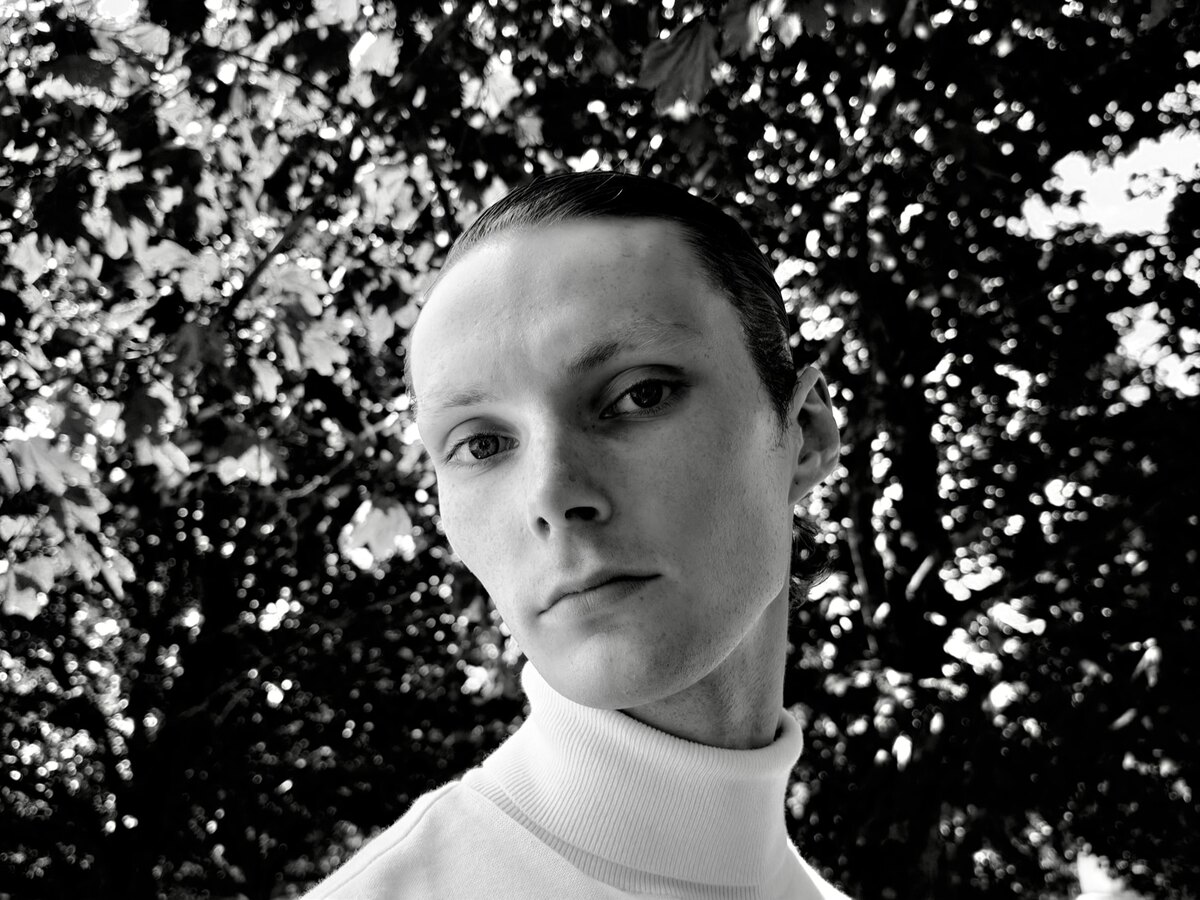 Black-and-white portrait taken on iPhone 18 Pro, the subject sharp against a blurred background of leaves