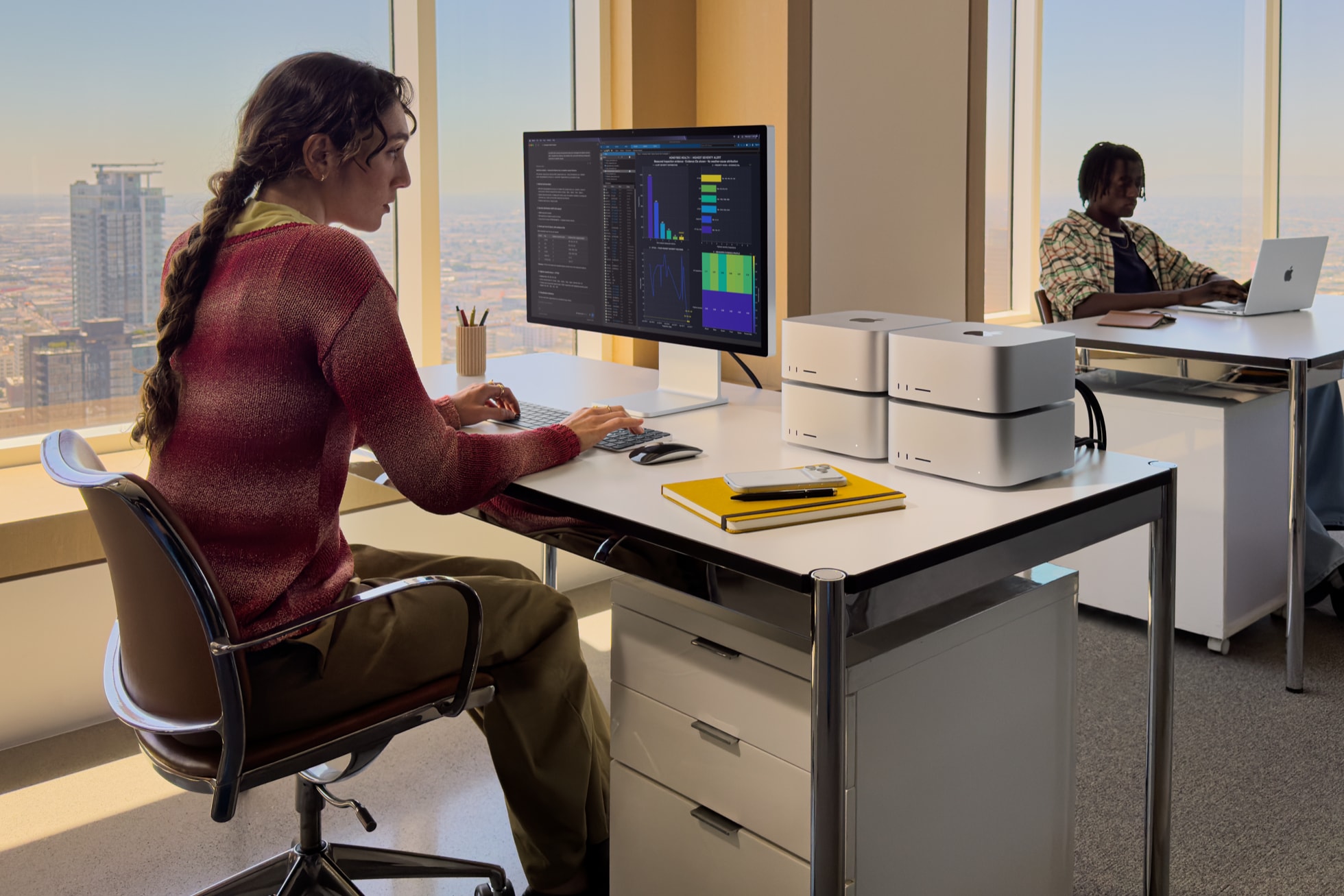 A person working at a desk with two Mac Studio computers and a display in a high-rise office